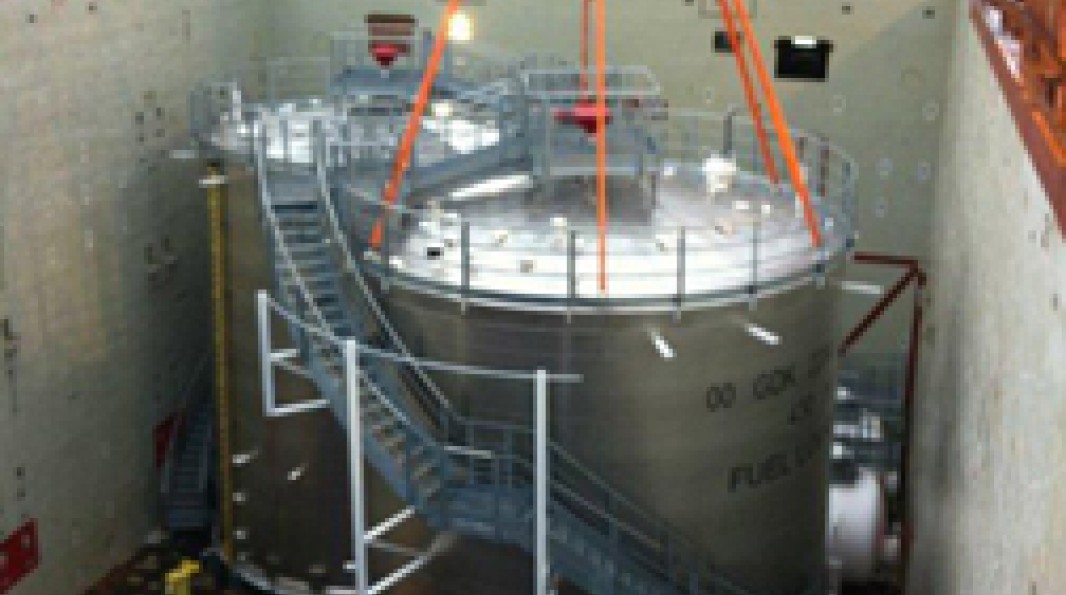 Photo de la mise en place dans une fosse d’un grand réservoir cylindrique, équipé d’escaliers et d’une plateforme, en phase d’installation