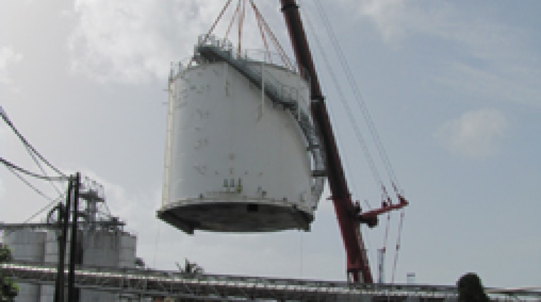 Photo du transport aérien d’un réservoir par une grue sur le site de la centrale, au milieu d’autres infrastructures industrielles